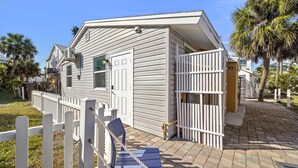 A single-story house with a white exterior, a front porch with a white picket fence, and a small blue chair.