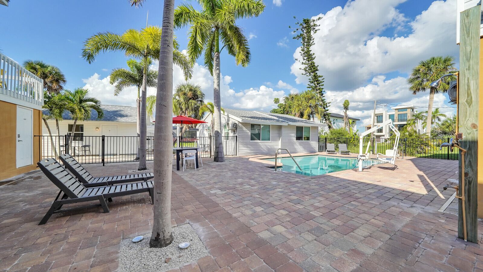 A pool area with lounge chairs, a red umbrella, and a small pool.