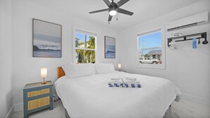Une chambre à coucher avec un lit, deux fenêtres, un ventilateur de plafond et un porte-serviettes fixé au mur.
