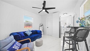 Un salon moderne avec un canapé bleu, des fauteuils gris et un coin repas comprenant des chaises noires et une table.