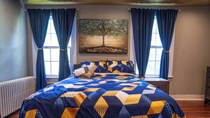 Un dormitorio con cama, ventana, radiador y un cuadro de un árbol.