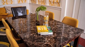 Una mesa de comedor con superficie de mármol, rodeada de sillas amarillas, y un libro titulado 'Dream Big' encima.