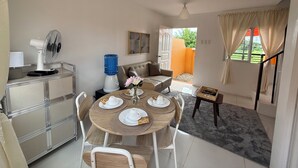 A dining area with a table set for four, a water dispenser, a fan, and a view of an outdoor balcony.