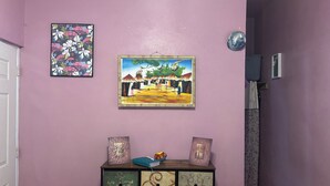 Een gang met een paarse muur, een houten kast met decoratieve lades, en twee ingelijste kunstwerken.
