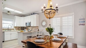 A dining area with a wooden table set for four, white cabinets, a kitchen in the background, and a chandelier. - Only 3 minutes walk to beach - Spacious Destin Home, Newly-renovated (Destin)