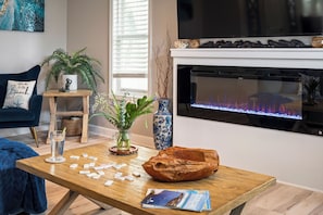 A living room with a fireplace, a television, a coffee table with dominoes, and a blue sofa. - Only 3 minutes walk to beach - Spacious Destin Home, Newly-renovated (Destin)