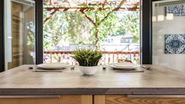 A dining table with two plates and a potted plant in the center, set against a backdrop of a wooden pergola and a view of greenery. - Whitewater Lodge-4units*nearDT (Boise)