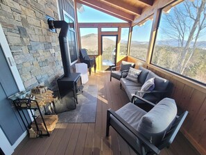 Una terraza de madera con un muro de piedra, una chimenea y una zona de estar con cojines.