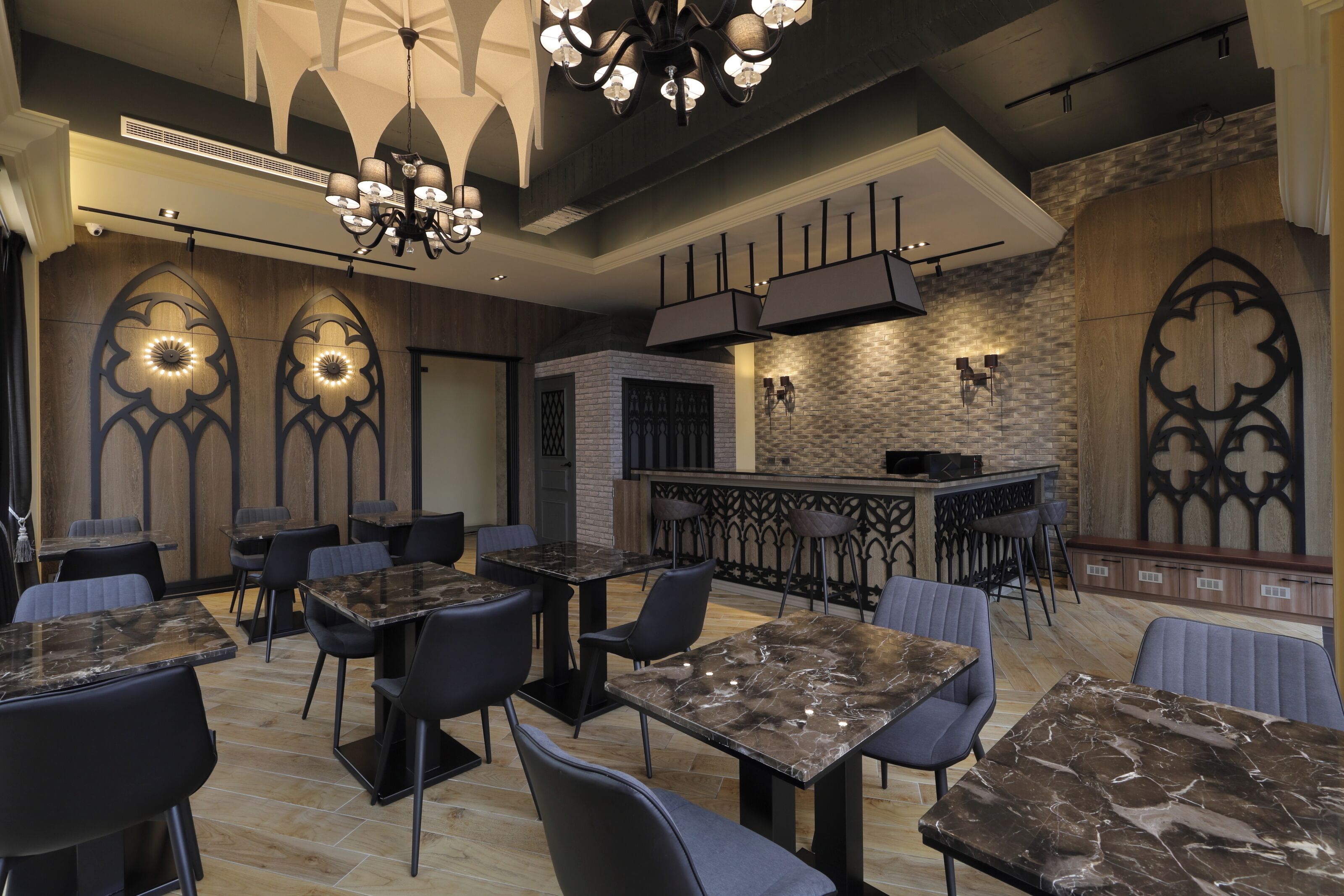 L’intérieur d’un restaurant avec des tables en marbre, des chaises noires et un coin bar dont le mur arrière est en pierre.