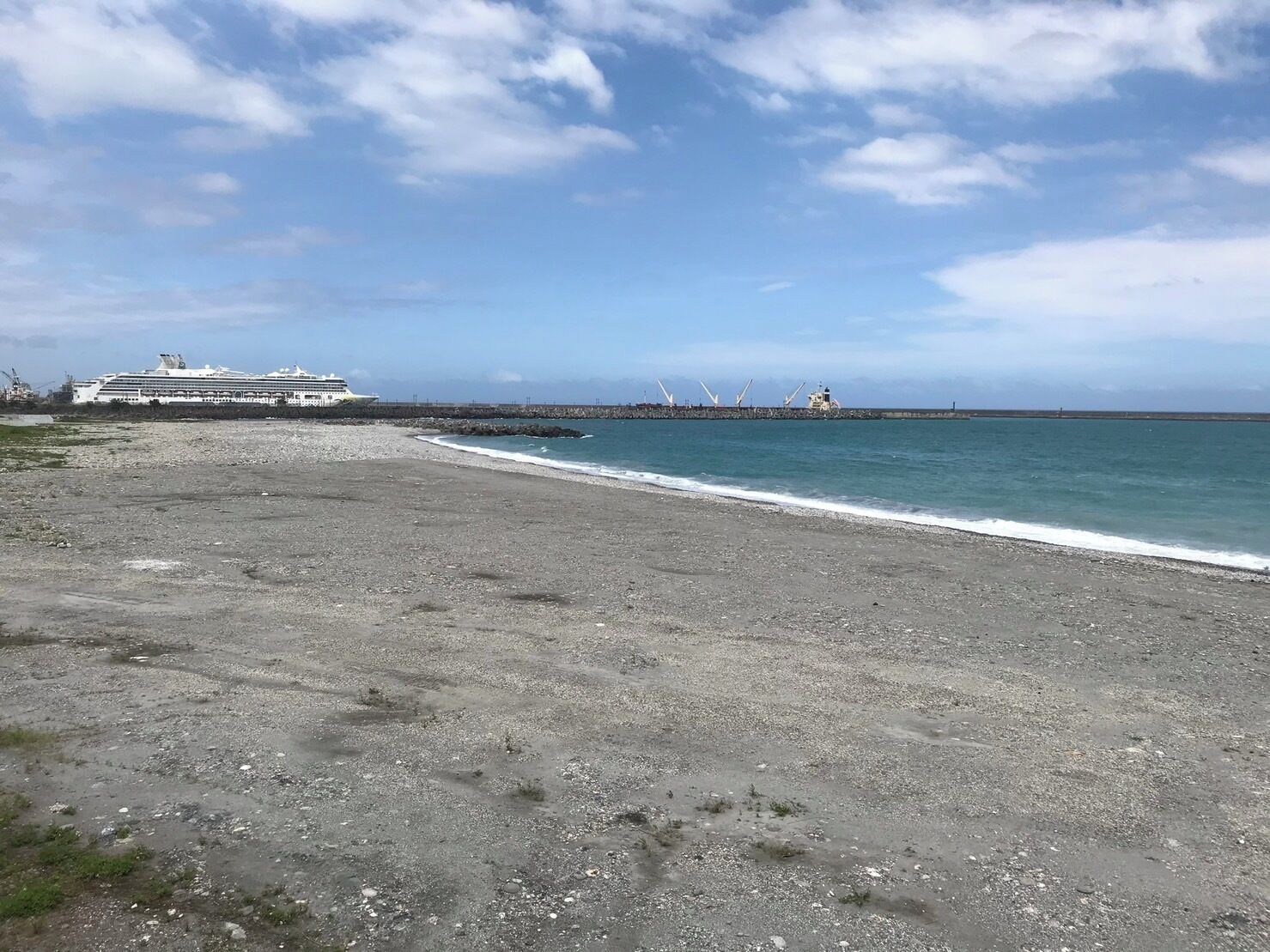 Una playa con un crucero atracado en un muelle, un faro y turbinas eólicas a lo lejos.