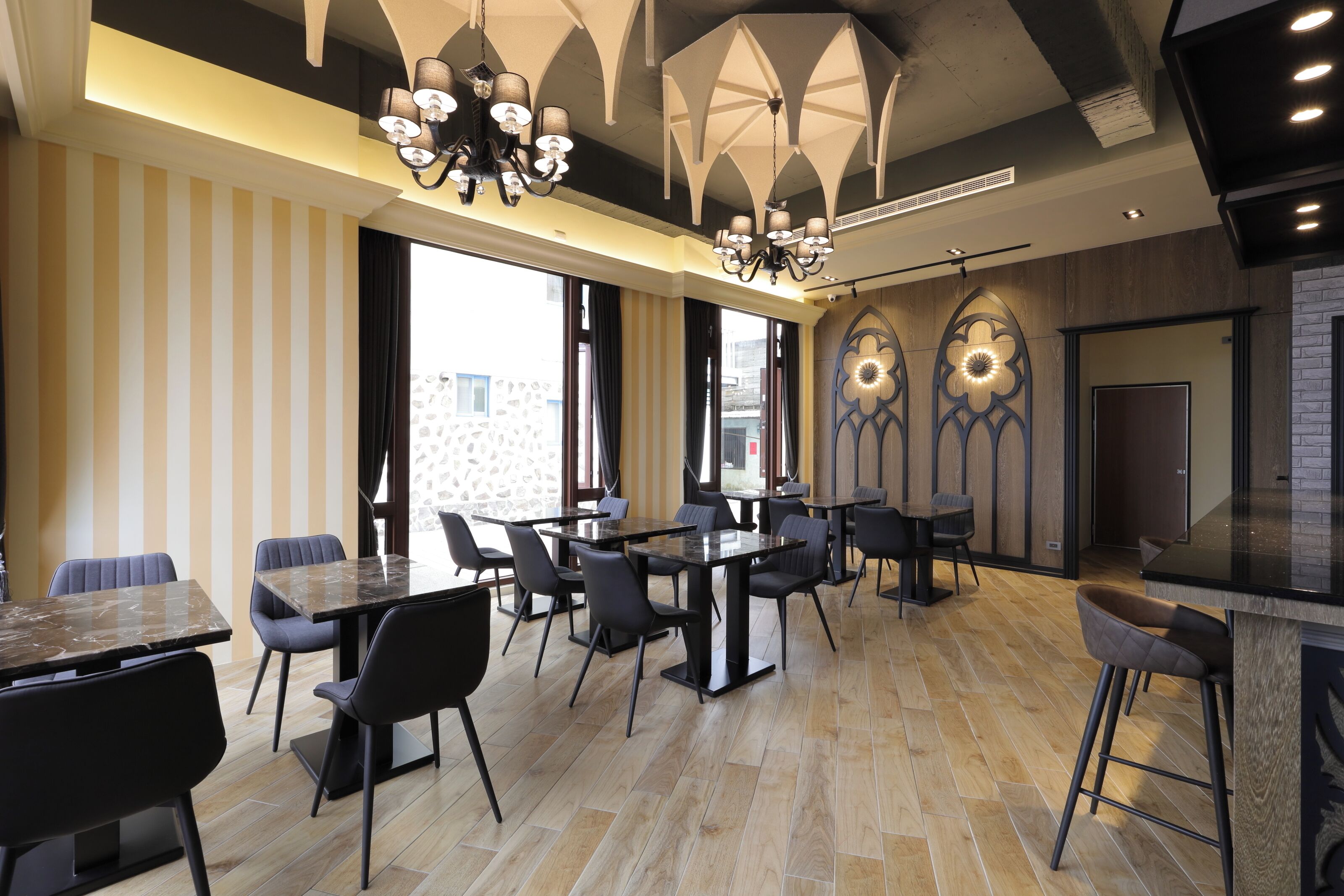 A modern dining area with multiple tables and chairs, large windows, and decorative lighting fixtures.