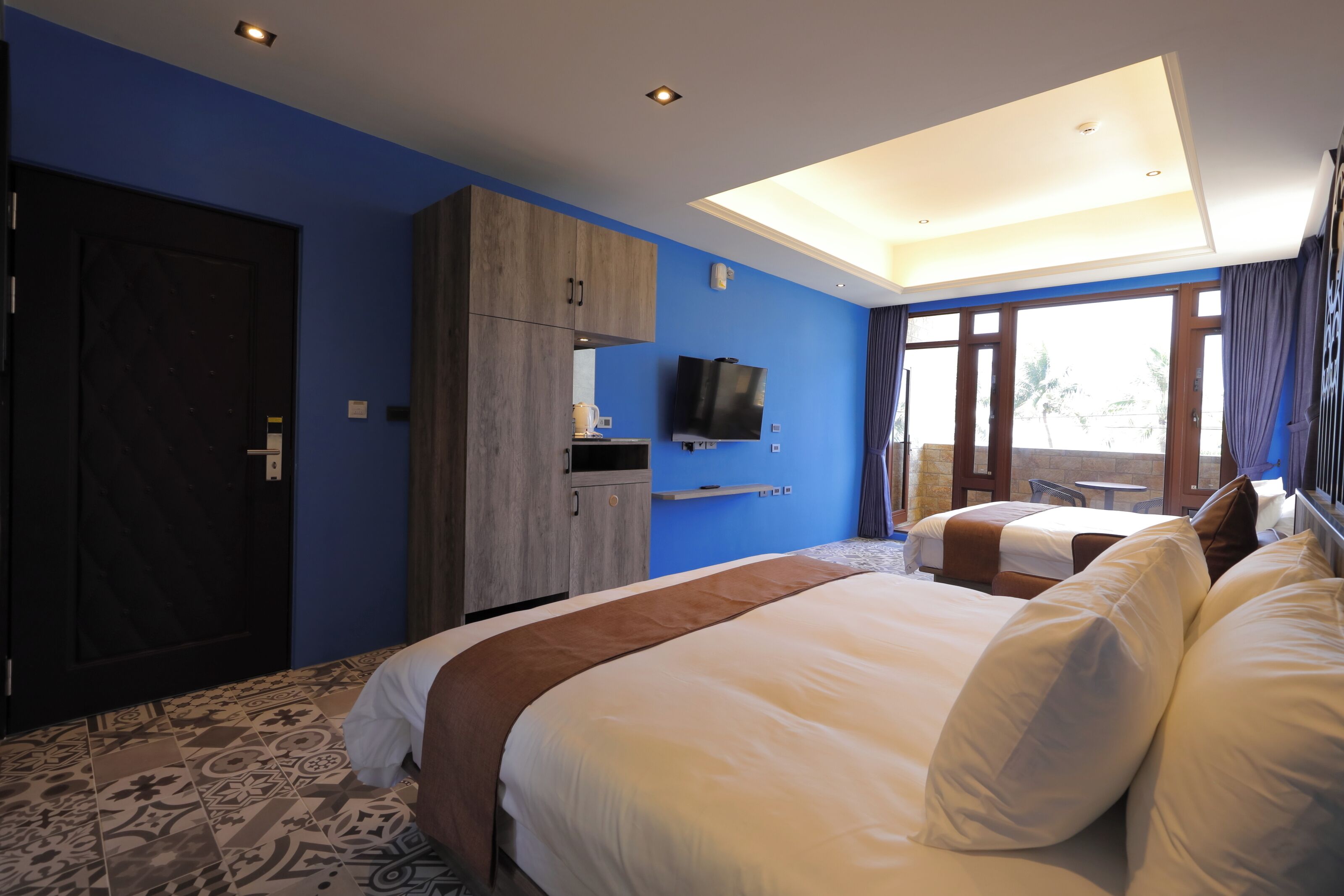 Habitación de hotel con dos camas, televisión, armario y balcón con vistas.