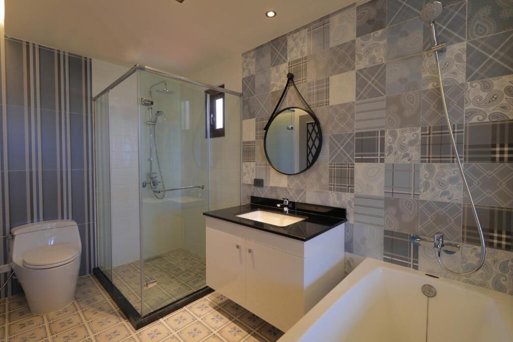A modern bathroom with a glass-enclosed shower, a white sink, and patterned tiles.