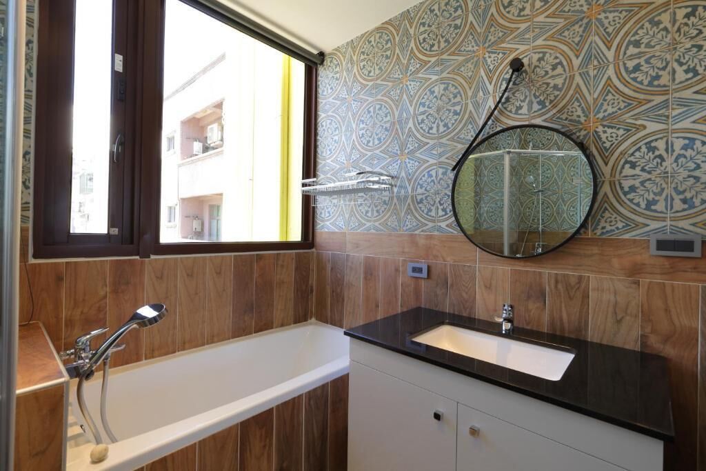 Un baño con bañera, lavabo, espejo y azulejos estampados.
