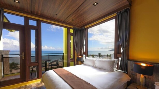 A hotel room with a large bed, a view of the ocean, and a balcony with a table and chairs. - Nottingham Seaview B&B (Hualien City)