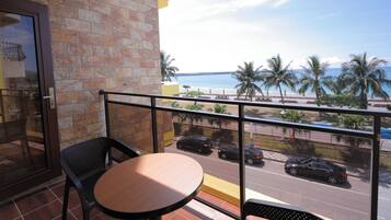 A balcony with a table and chairs, overlooking a beach and a road with cars.