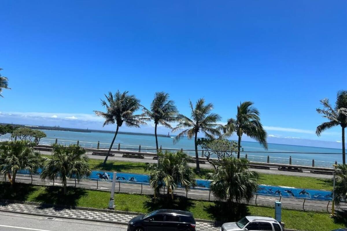 A coastal road with palm trees, a swimming pool, and a view of the ocean.