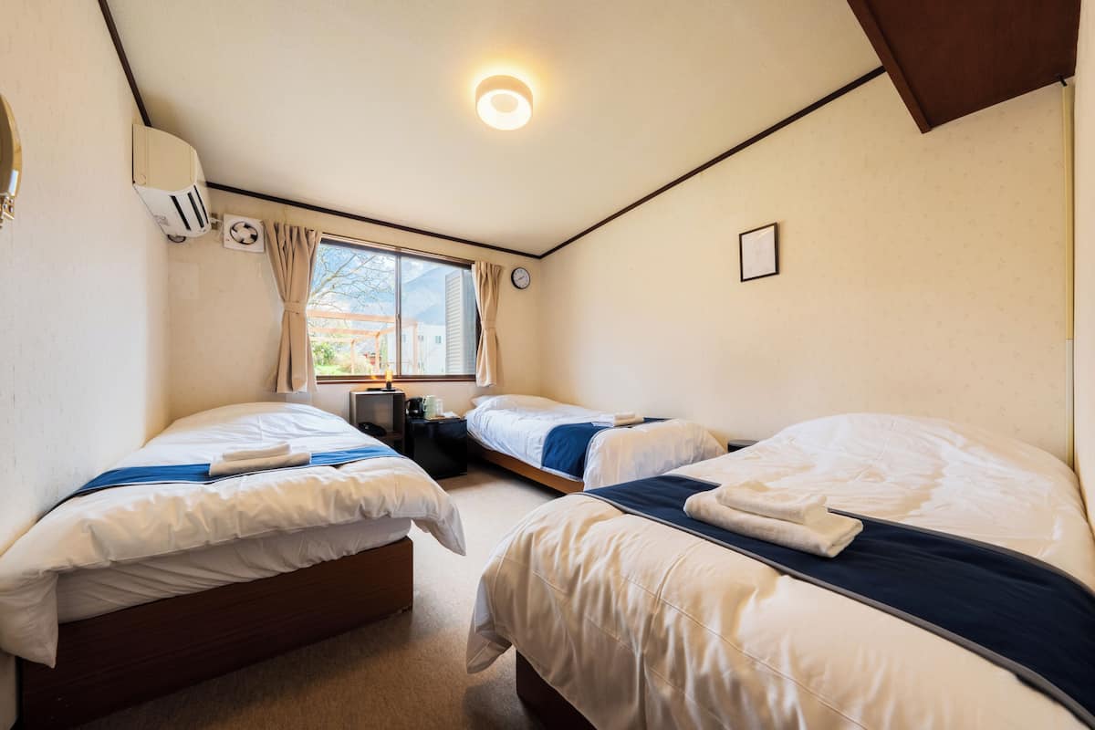 Una habitación con dos camas, una ventana, un reloj y un equipo de aire acondicionado.