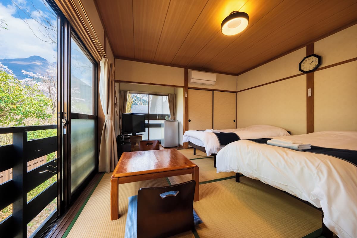 Habitación de hotel con dos camas, una mesa de madera, televisión y vista a los cerezos en flor.