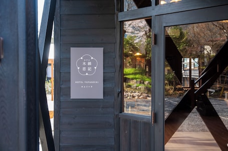 A wooden wall with a sign for Hotel Yufuogiiki, a wooden staircase, and a view of a garden.