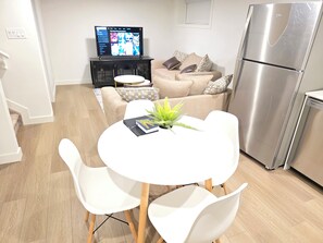 Una cocina moderna con un refrigerador de acero inoxidable, una mesa de comedor con sillas blancas y un televisor sobre un mueble negro.