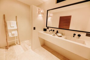 Une salle de bain moderne avec un grand miroir, une échelle en bois et un lavabo blanc agrémenté d’articles de toilette.