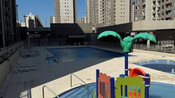 Ein Poolbereich auf dem Dach mit einer Spielanlage für Kinder, umgeben von Hochhäusern.