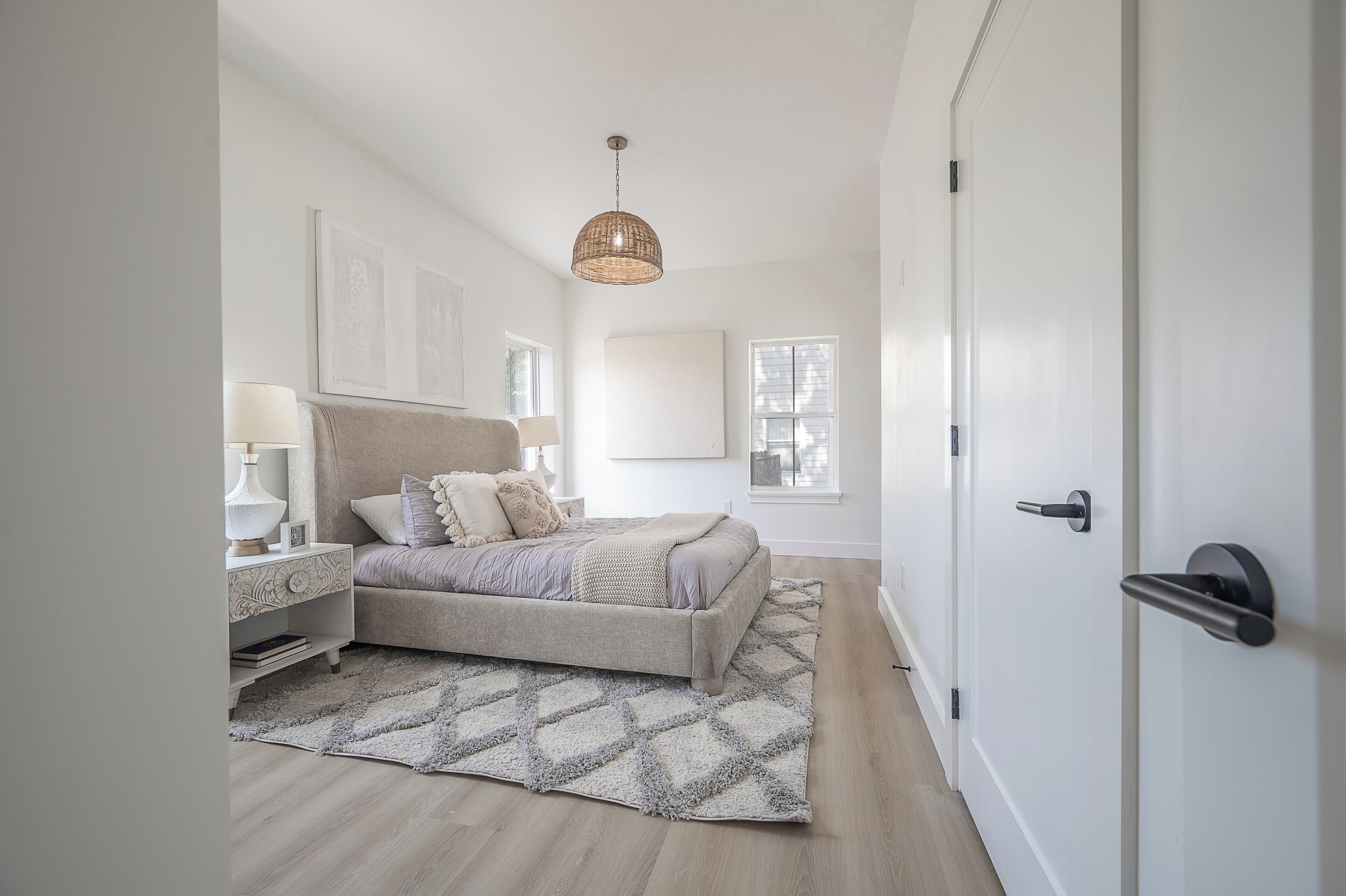 A bedroom with a bed, bedside tables, a hanging light fixture, and a door.