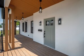 Ein überdachter Veranda mit Holzbalken, einer weißen Außenwand und einer grünen Tür.