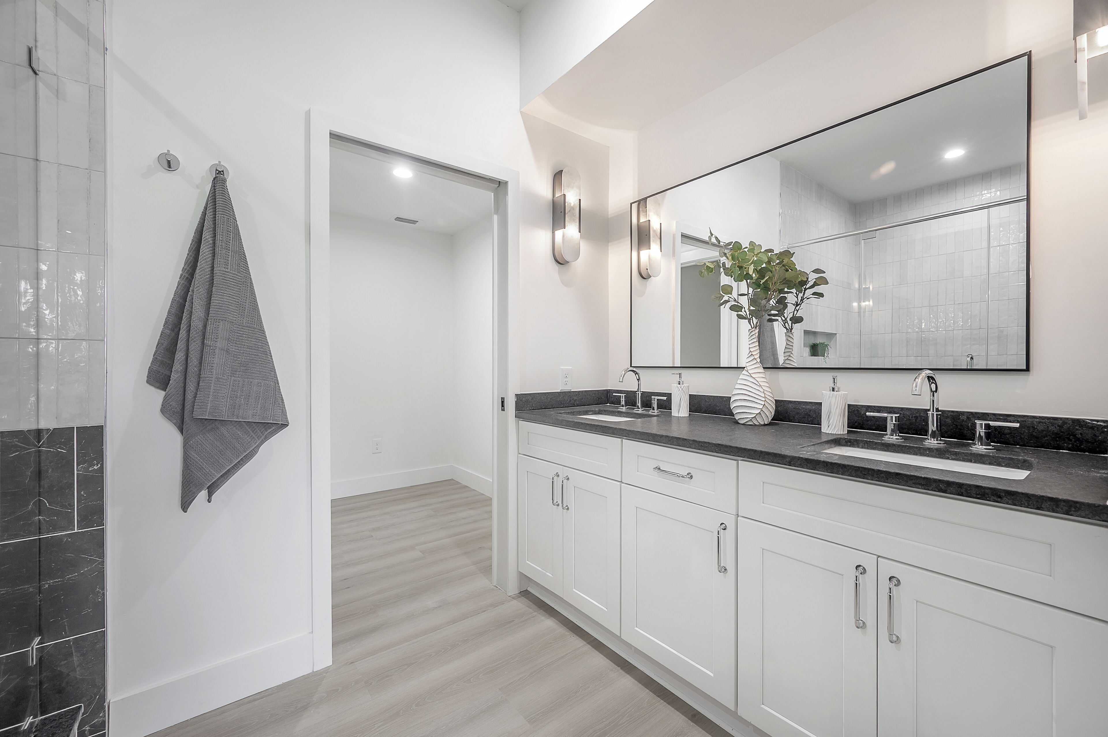 A modern bathroom with a large mirror, white cabinets, a black countertop, and a towel hanging on the wall.