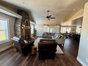 A spacious living room with a stone fireplace, leather sofas, and a dining area with wooden chairs.