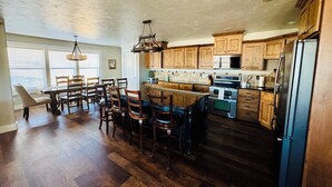 A kitchen with wooden cabinets, a central island, a dining area with chairs, and a refrigerator. - Awesome 6-bedroom house with rec room, fully equipped kitchen, Near Lava (McCammon)