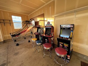 A room with a basketball arcade game, a hammock, and two stools.
