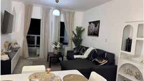 Un soggiorno moderno con un divano nero, un tavolo da pranzo con centrotavola decorativi e un'ampia finestra con tende.