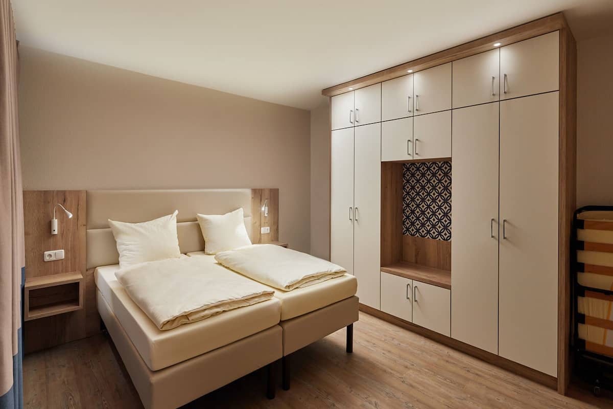 A bedroom with a bed, wooden wardrobe, bedside tables, and a nightstand.