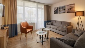 A modern living room with a sofa, armchair, and coffee table. There is a lamp, a TV, and a radiator.