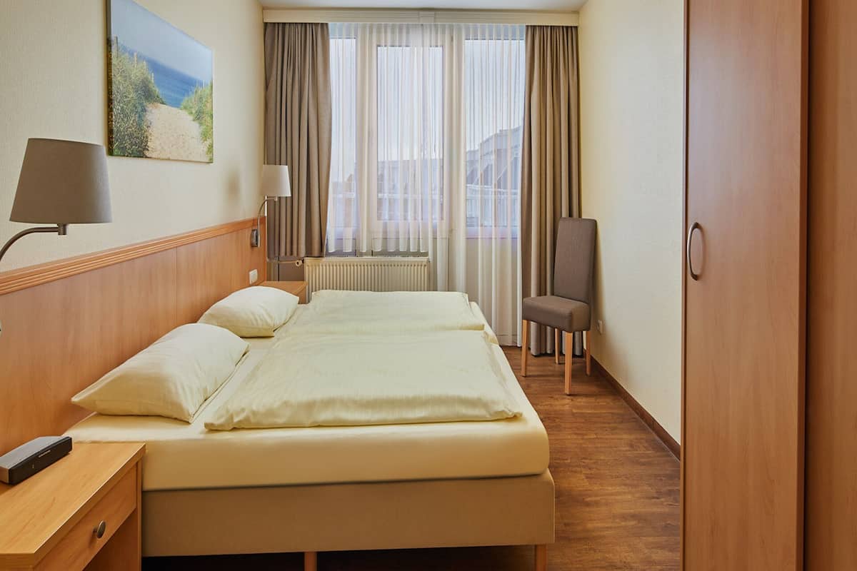 A hotel room with a large bed, a chair, a desk, and a window with curtains.