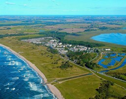 An aerial view of a coastal town with a beach, residential buildings, and a park with ponds.