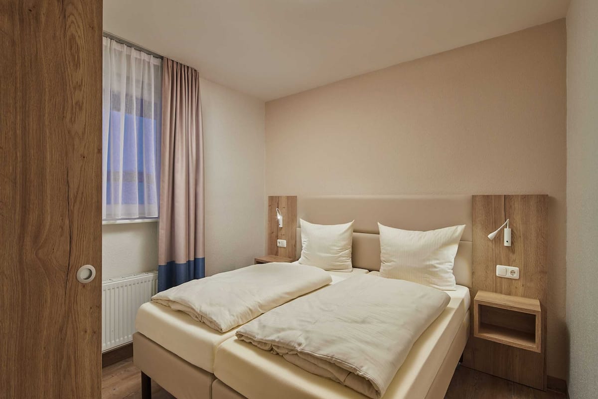 A double bed with a wooden headboard, two bedside tables, a nightstand, and a window with curtains.