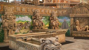 A stone fountain with a lion head, surrounded by stone carvings and a mural of a temple.