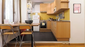 Eine kleine Küche mit Holzschränken, einem Einbauofen und einem Spülbecken. Zwei Stühle und ein kleiner Tisch sind ebenfalls vorhanden.