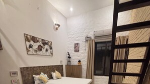 A bedroom with a bed, a small table, a chair, a wardrobe, and a decorative wall piece. - Aranyaa Cottage Homestay, Vrindavan (Jait)