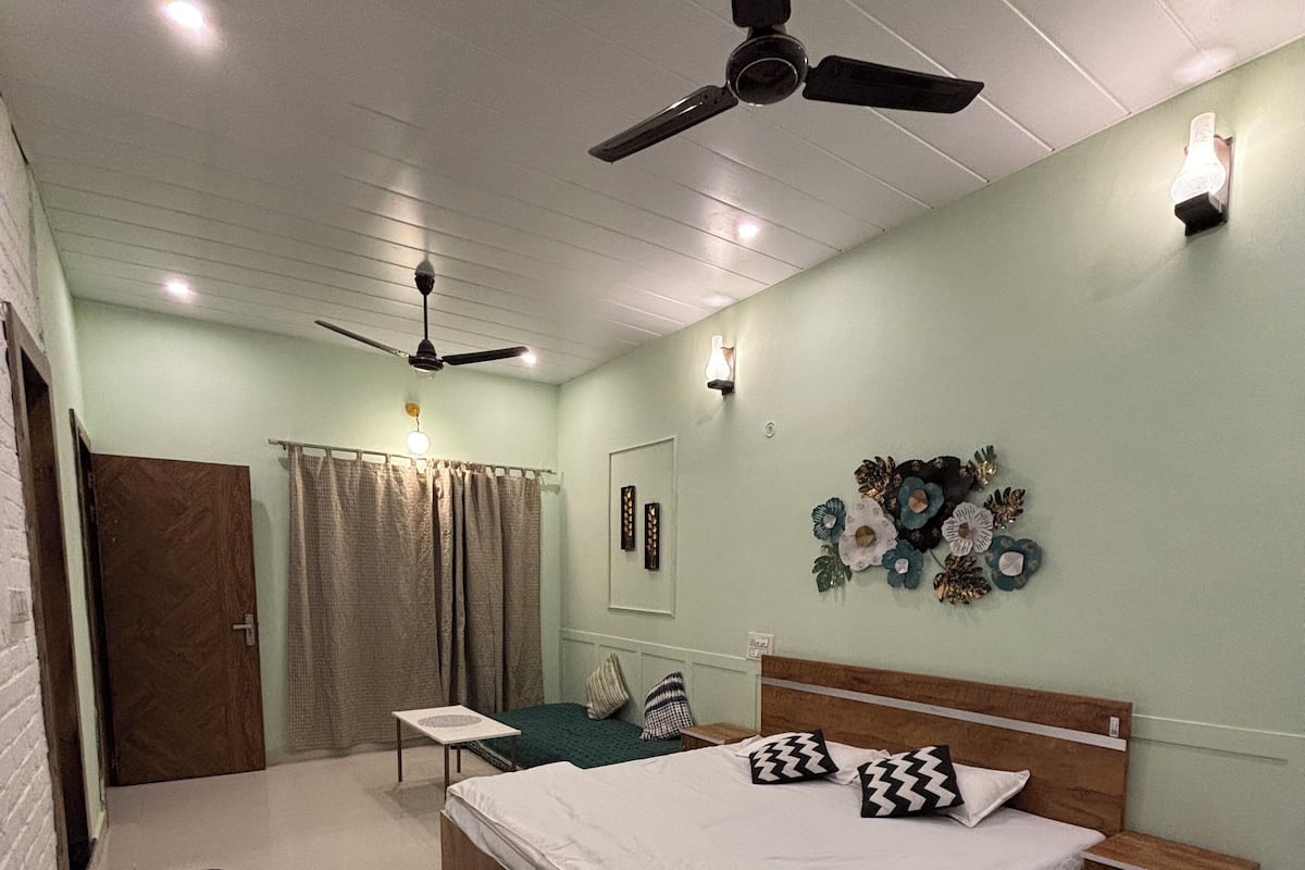 A bedroom with a bed, a nightstand, a ceiling fan, a wall-mounted light, a curtain, and a patterned rug.