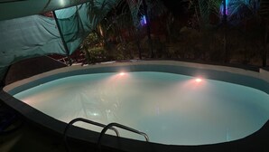 An indoor swimming pool with a clear water surface, surrounded by palm trees and a covered area with a green tarp. - Aranyaa Cottage Homestay, Vrindavan (Jait)