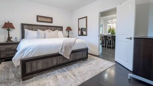 A modern bedroom with a large bed, bedside tables, a mirror, and a door leading to a bathroom. - Niagara 3BR w/ Huge Deck, King Suite, EV Charger & 5-Car Parking (St. Catharines)