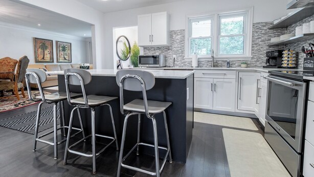 A modern kitchen with a central island, bar stools, and stainless steel appliances. - Niagara 3BR w/ Huge Deck, King Suite, EV Charger & 5-Car Parking (St. Catharines)