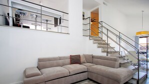 Una sala de estar moderna con un sofá modular en forma de L, una escalera con barandilla de metal y piso de madera.