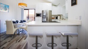 Una cocina moderna con armarios blancos, electrodomésticos de acero inoxidable y una isla central con taburetes de bar.
