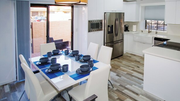 Una cocina moderna con armarios blancos, un refrigerador de acero inoxidable y un comedor con mesa dispuesta para seis comensales.