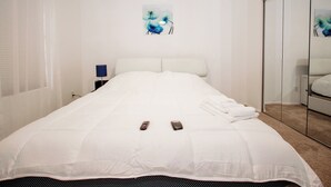 Una cama bien hecha con ropa blanca, un control remoto y un teléfono inteligente sobre la cama.